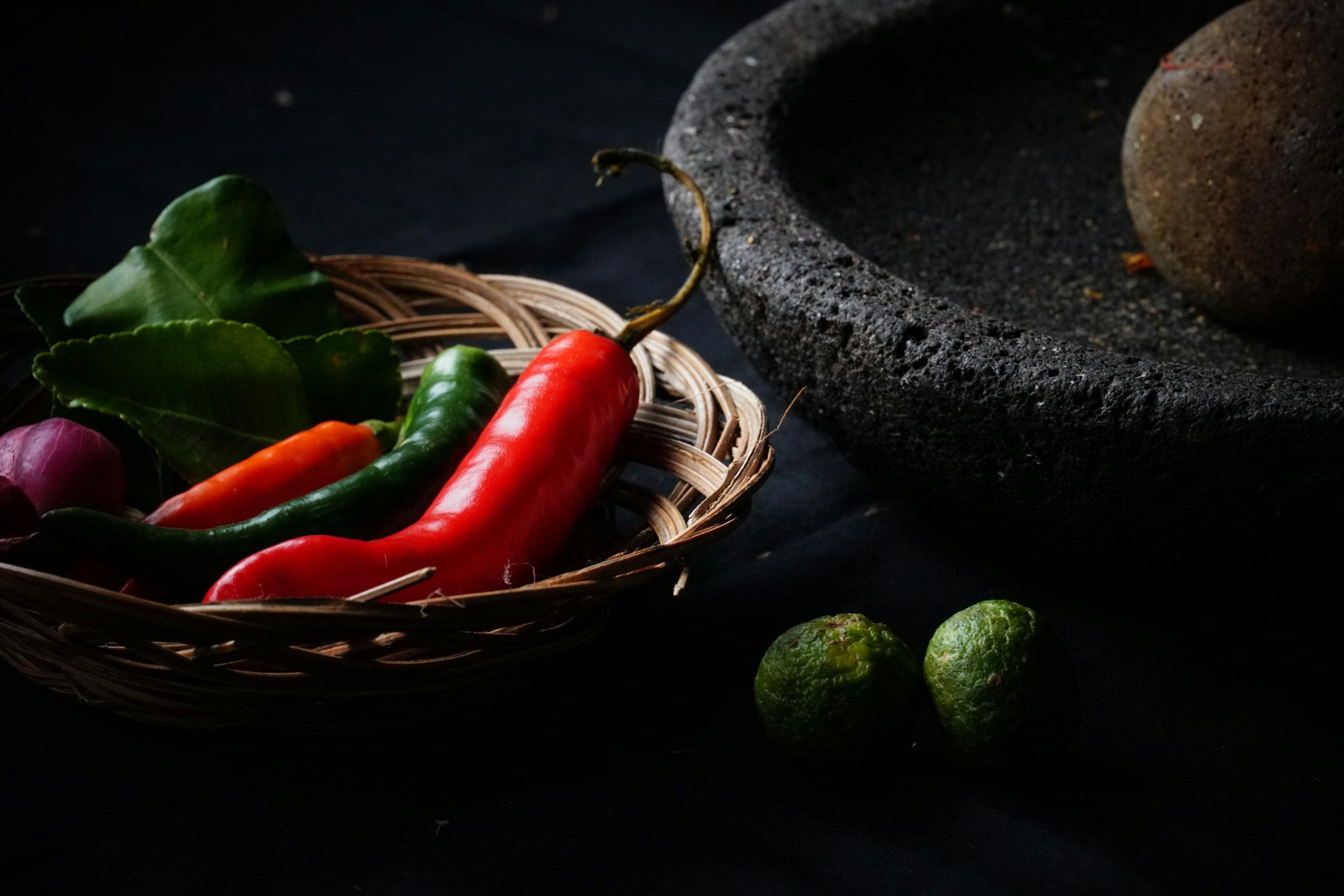 Fresh chillies, kaffir lime leaves, shallot and limes beside a stone mortar — the raw ingredients behind a Life's Good curry paste